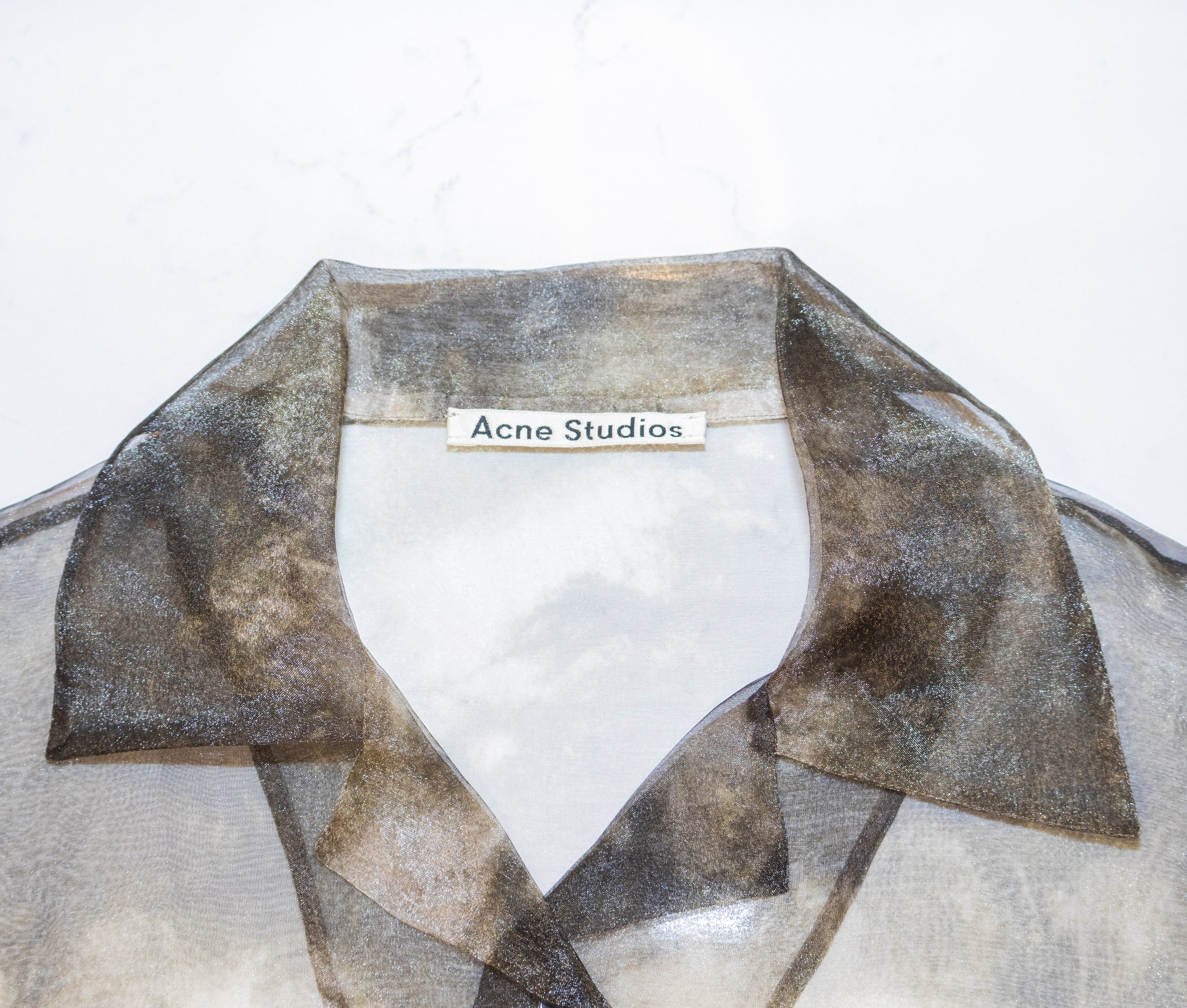 Close-up of a sheer organza shirt collar with a metallic bronze and gold shimmer, featuring an Acne Studios label at the inner neck.